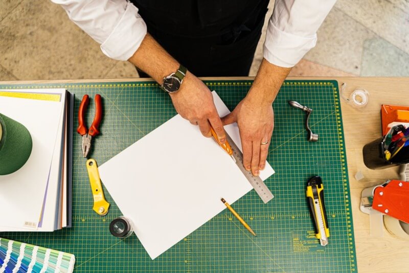 Artesão trabalhando em uma bancada usando uma régua e estilete para cortar o material