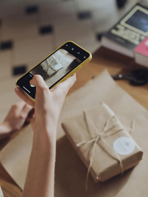 Artesã fotografando com o celular uma peça de artesanato embalada para divulgar no Instagram